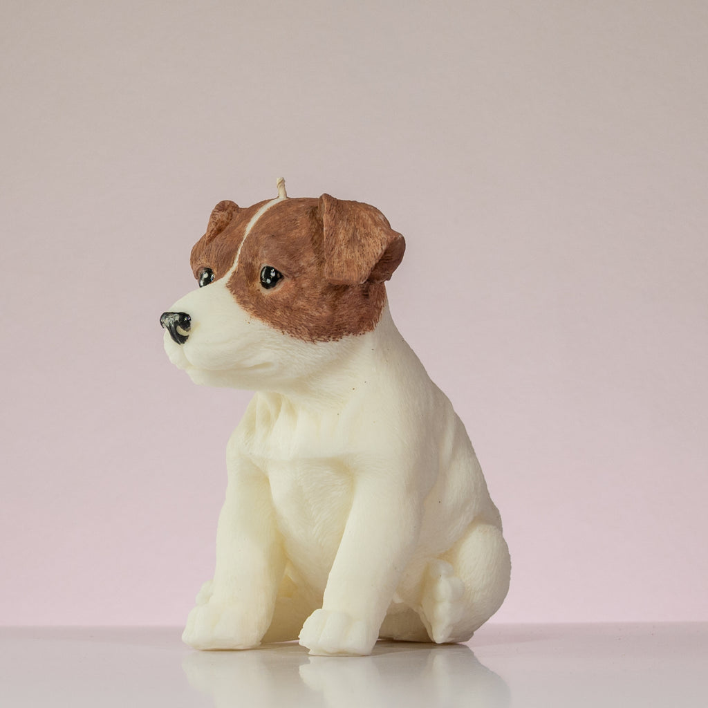 Luz Candles Au - A sculpted dog-shaped candle in the shape of a sitting puppy, with brown and white colouring, photographed on a plain light pink background.