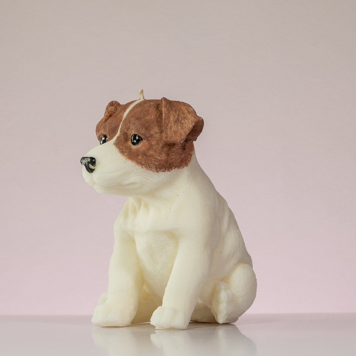 Luz Candles Au - A sculpted dog-shaped candle in the shape of a sitting puppy, with brown and white colouring, photographed on a plain light pink background.