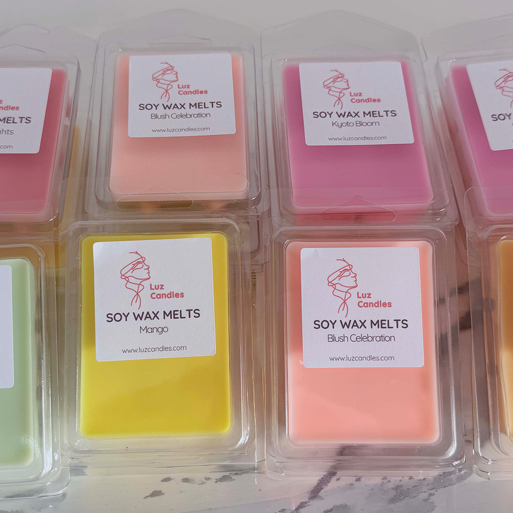 A grid of clear plastic clamshell packages containing colorful soy wax melts. Each package has a white label with the brand name 'Luz Candles' and scent names including 'Blush Celebration', 'Kyoto Bloom', and 'Mango'.