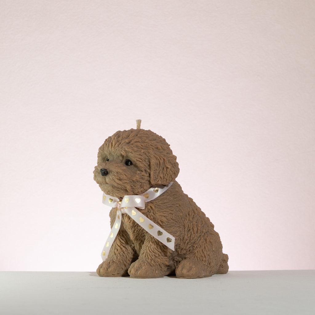 Brown poodle dog-shaped candle with a white ribbon on a light pink background