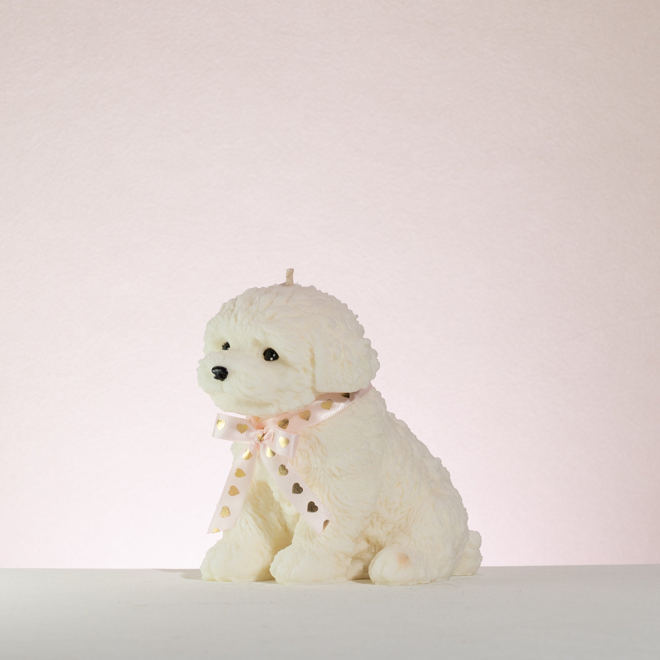 White poodle dog-shaped candle with a pink bow on a light pink background