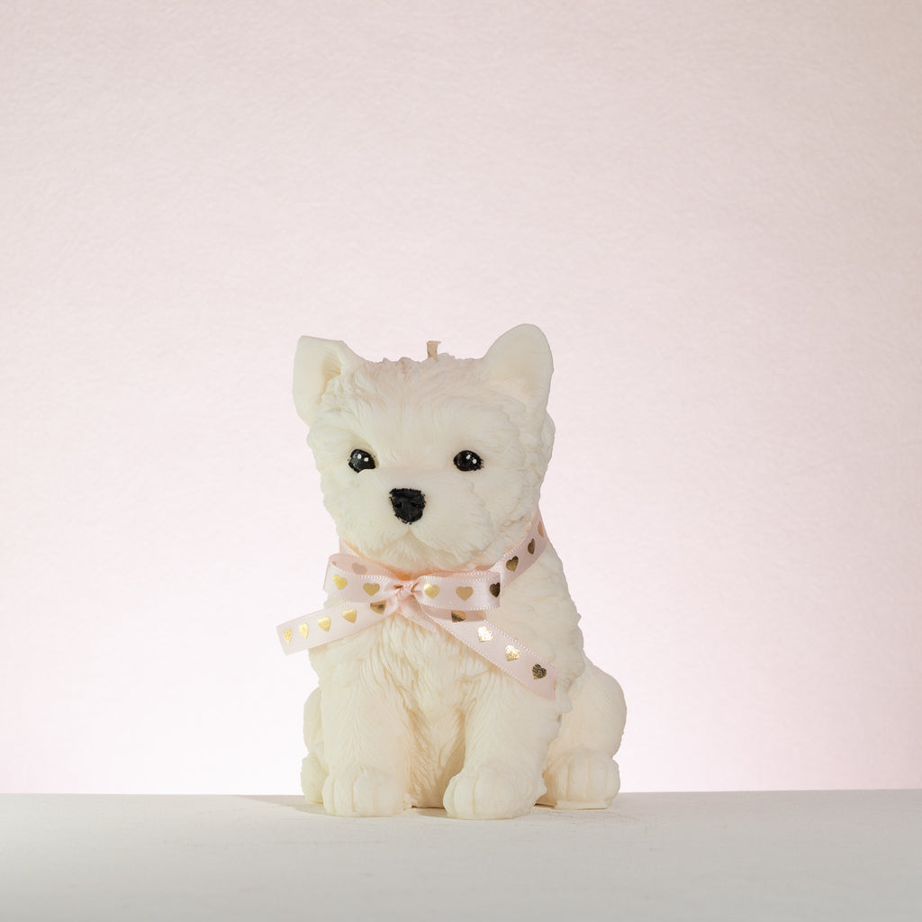 White westie dog-shaped candle with a pink bow on a white background