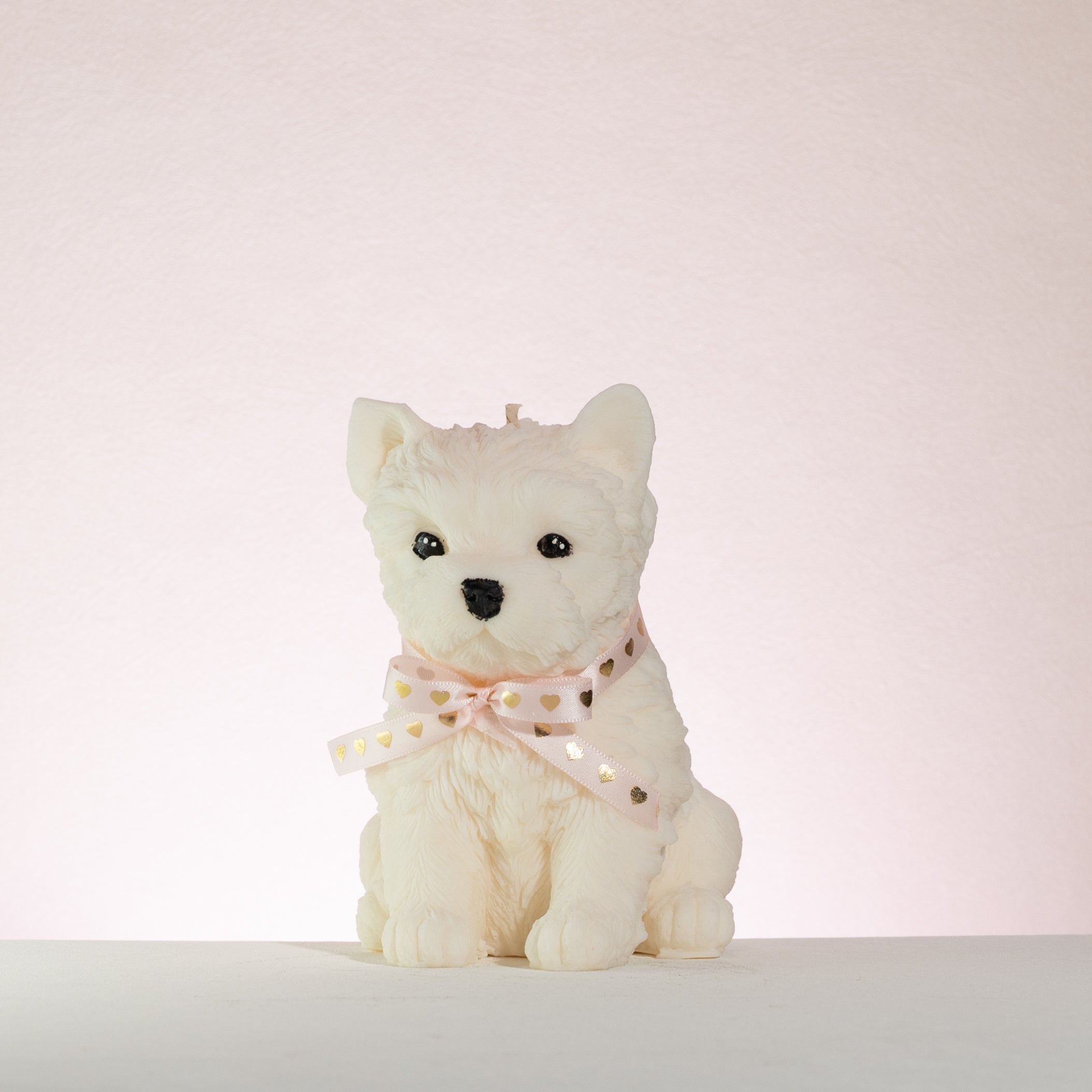 White westie dog-shaped candle with a pink bow on a white background