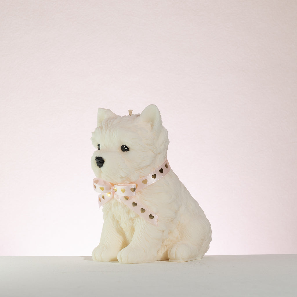 White dog-shaped candle with a pink heart collar on a light pink background