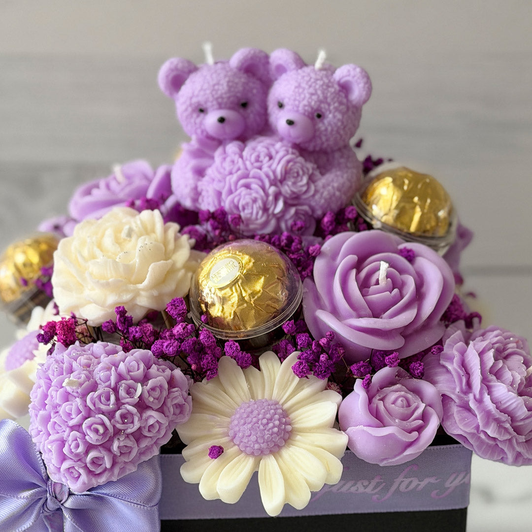 Decorative arrangement with purple teddy bears, flowers, and chocolates on a light grey background