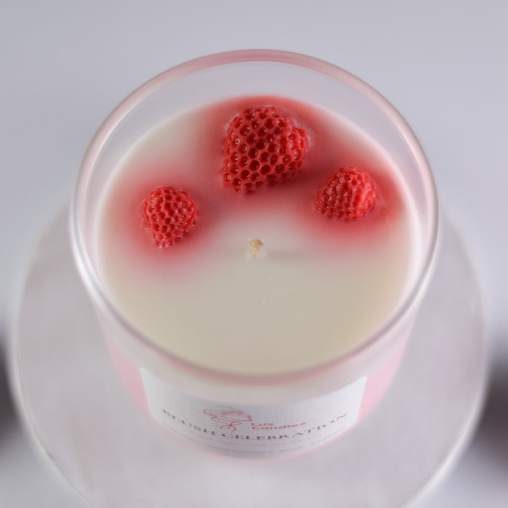 Candle with red strawberry-shaped decoration on top on a white plate