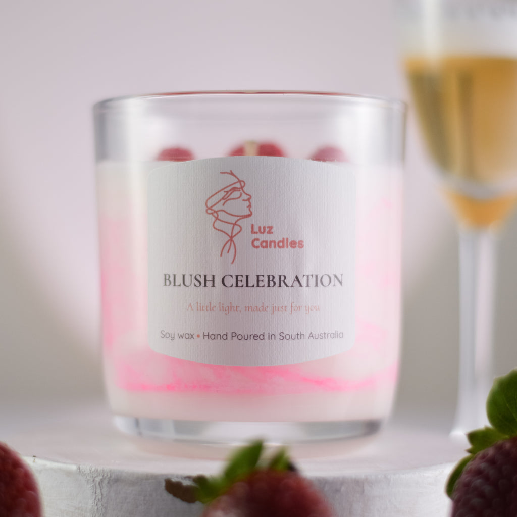 Luz Candles Blush Celebration candle with a blurred glass of wine and strawberries in the background.