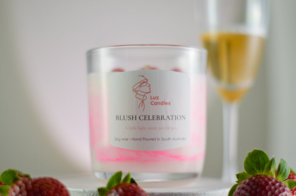 Luz Candles Blush Celebration candle with a glass of champagne and strawberries in the background.