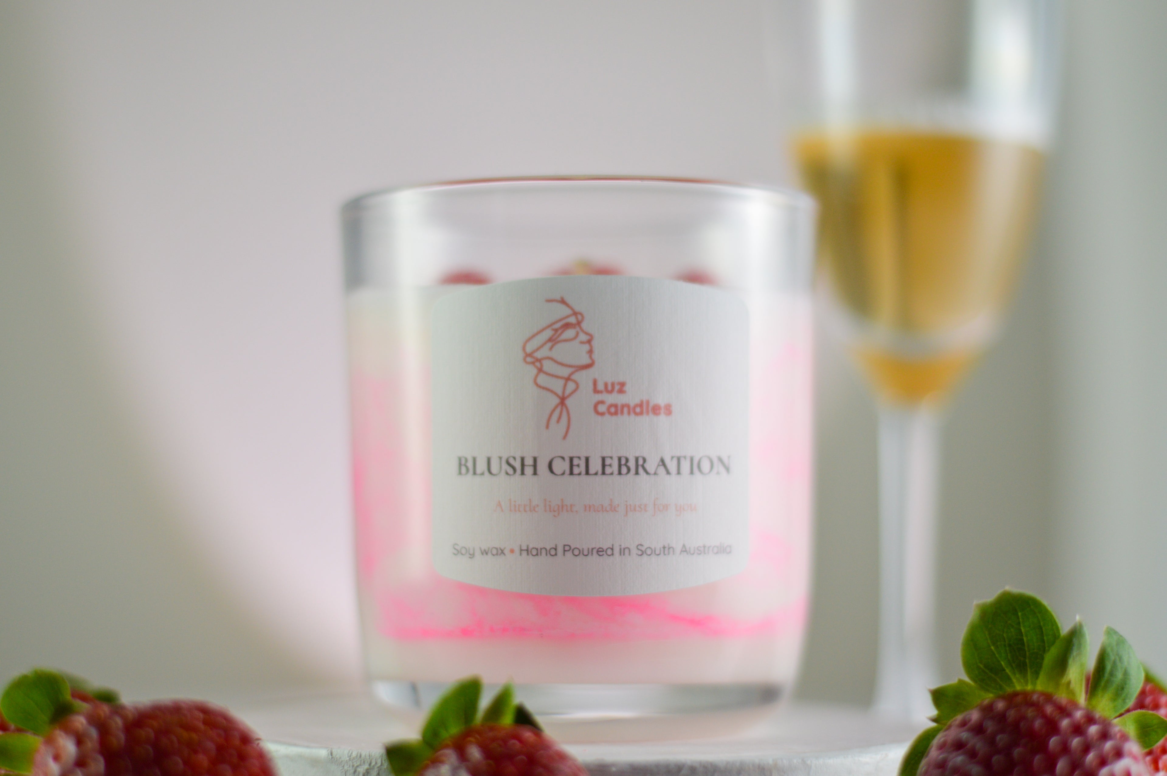 Luz Candles Blush Celebration candle with a glass of champagne and strawberries in the background.