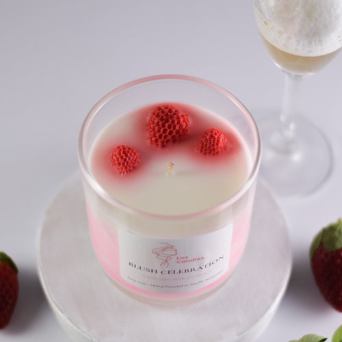 Candle with strawberry decorations on a white surface, next to a glass of dessert.