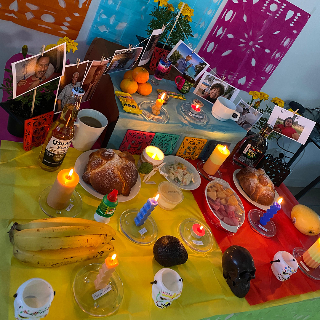 Decorative table with food, drinks, and candles on a colourful tablecloth representing Day of the Dead.