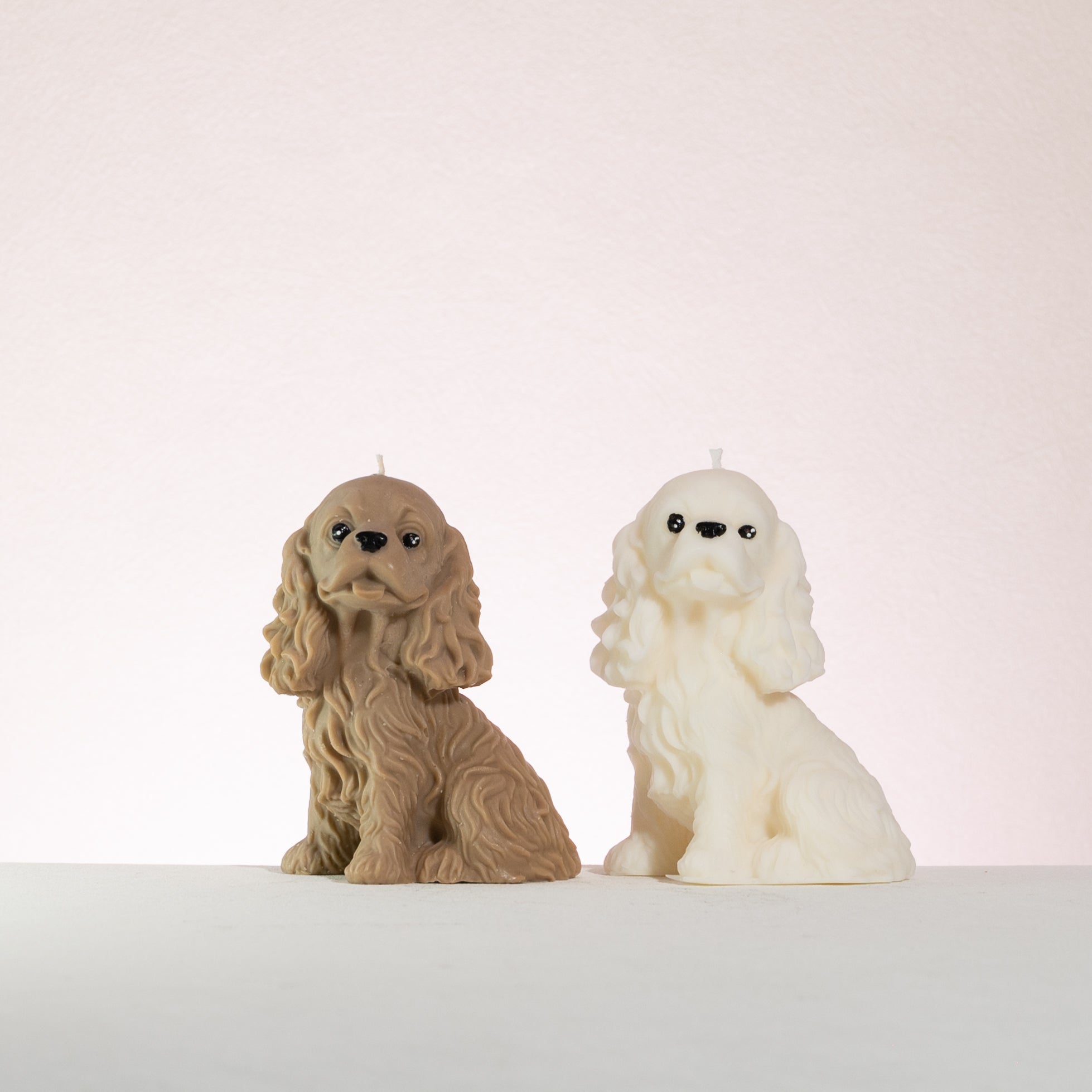 Two cocker spaniel dog-shaped candles, one brown and one white, on a light background