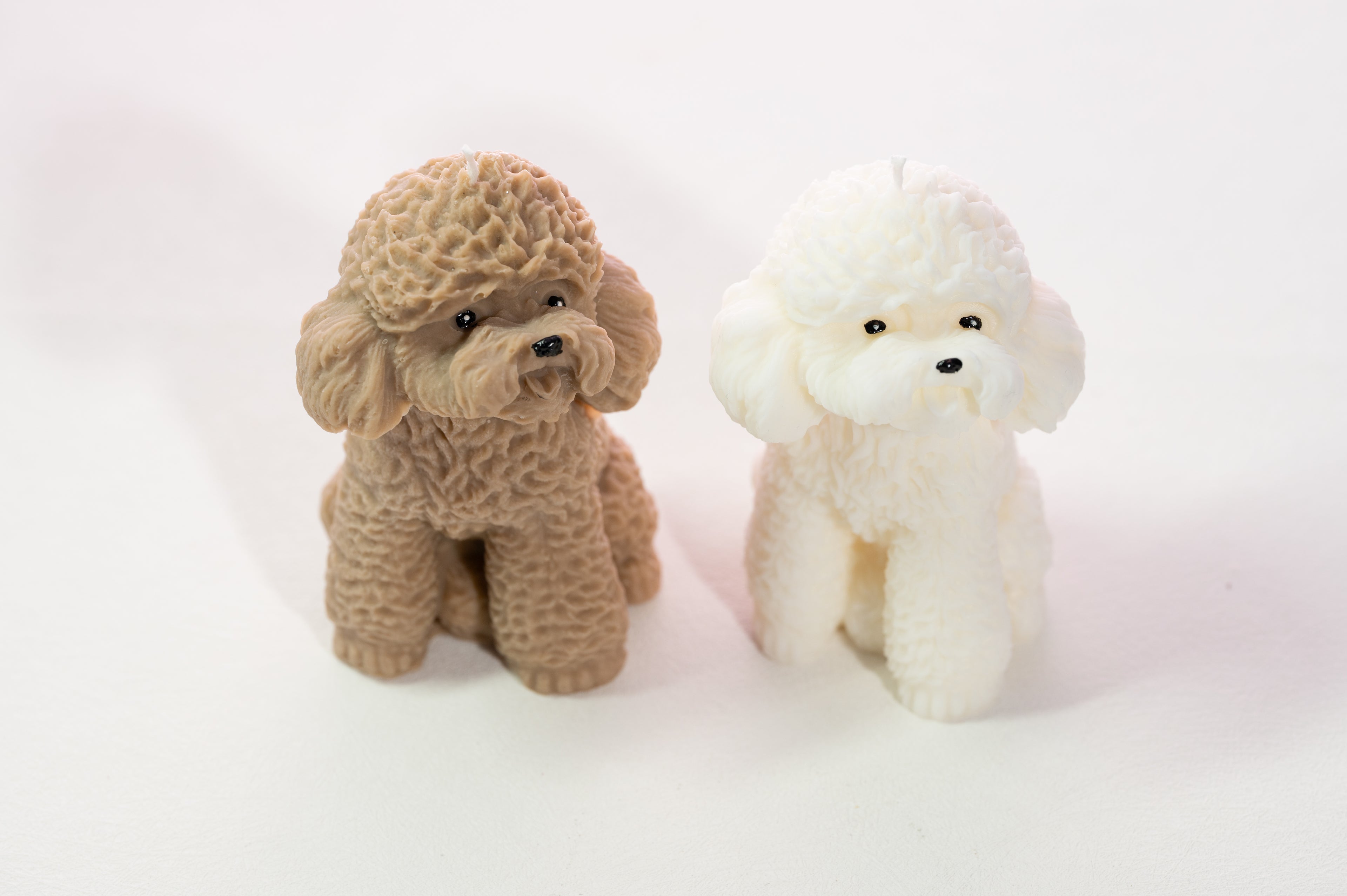 Two scented candle poodles, one brown and one white, on a light pink background