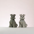 Two schnauzer dog-shaped candles on a white surface with a light pink background
